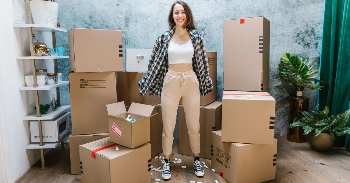 Femme souriante entourée de cartons prêts pour le jour du déménagement dans une maison moderne élégante.