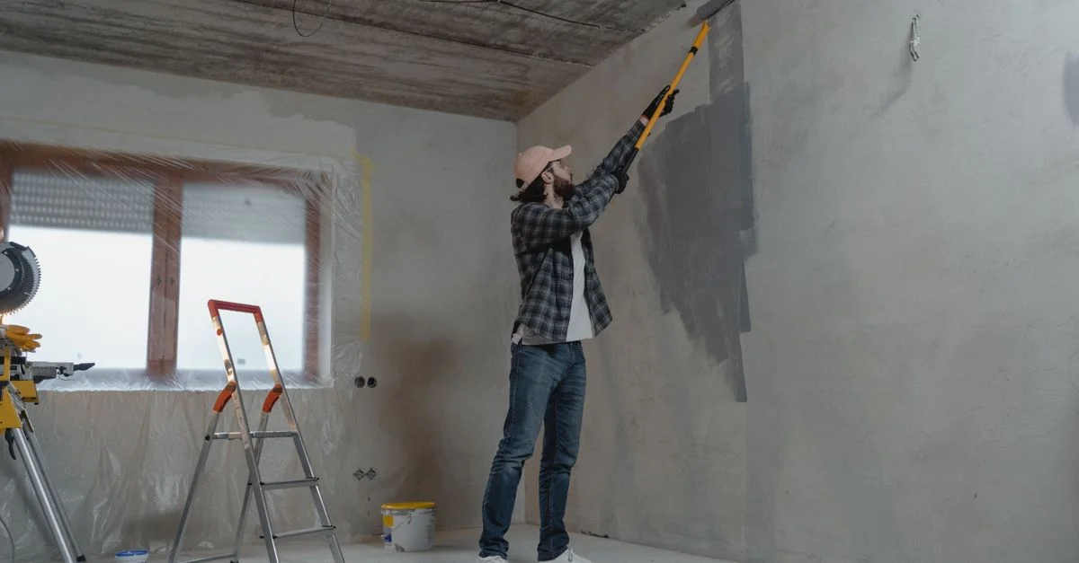 Un homme peignant un mur intérieur avec un rouleau pendant un projet de rénovation domiciliaire.