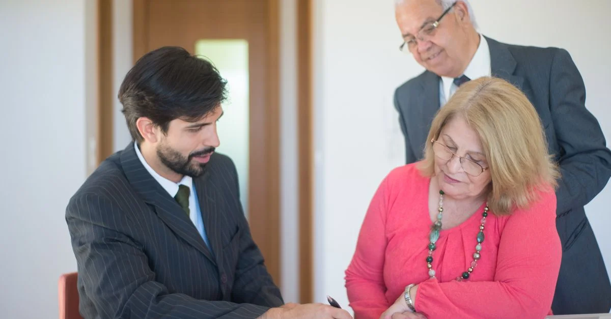 Couple senior signant des documents immobiliers avec un agent dans un bureau moderne.