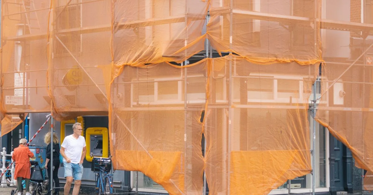 Scène de rue montrant la façade d'un bâtiment en rénovation avec des piétons.