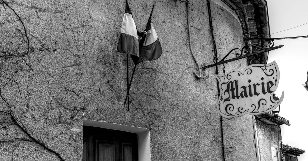 Photo en noir et blanc de la façade d'une mairie française, ornée de drapeaux et empreinte de nostalgie.