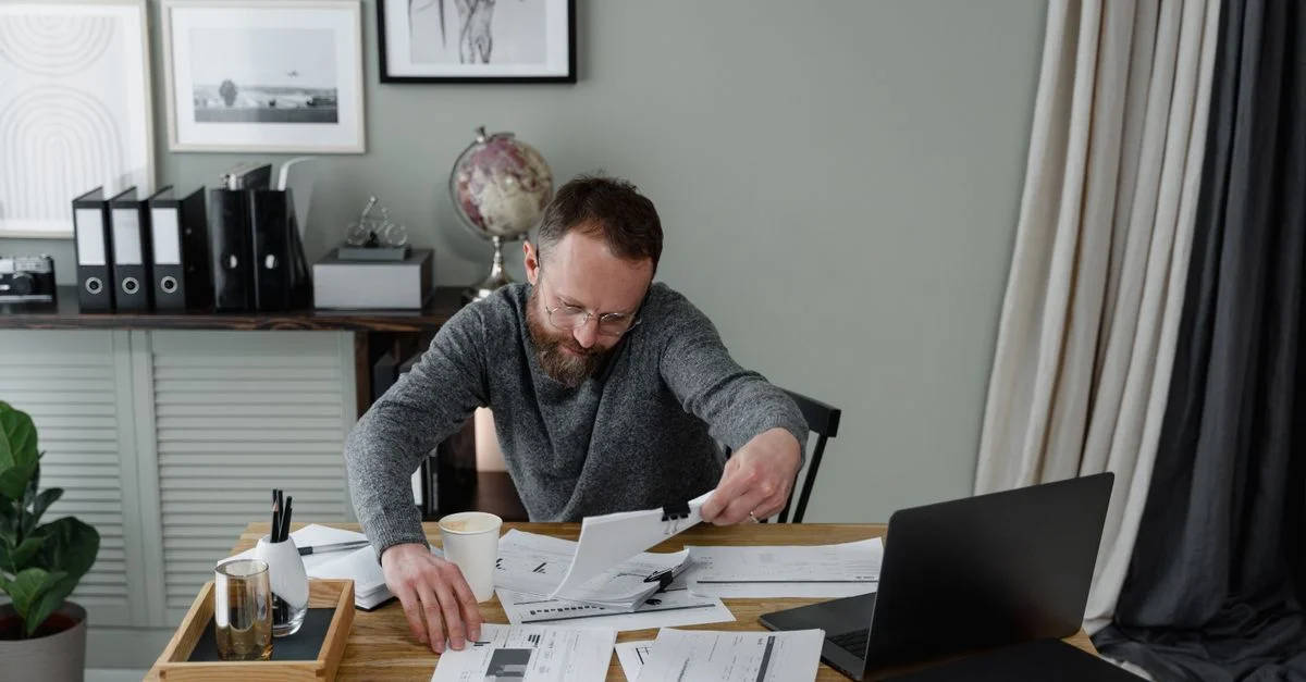 Professionnel examinant des documents à un bureau avec un ordinateur portable et du café.