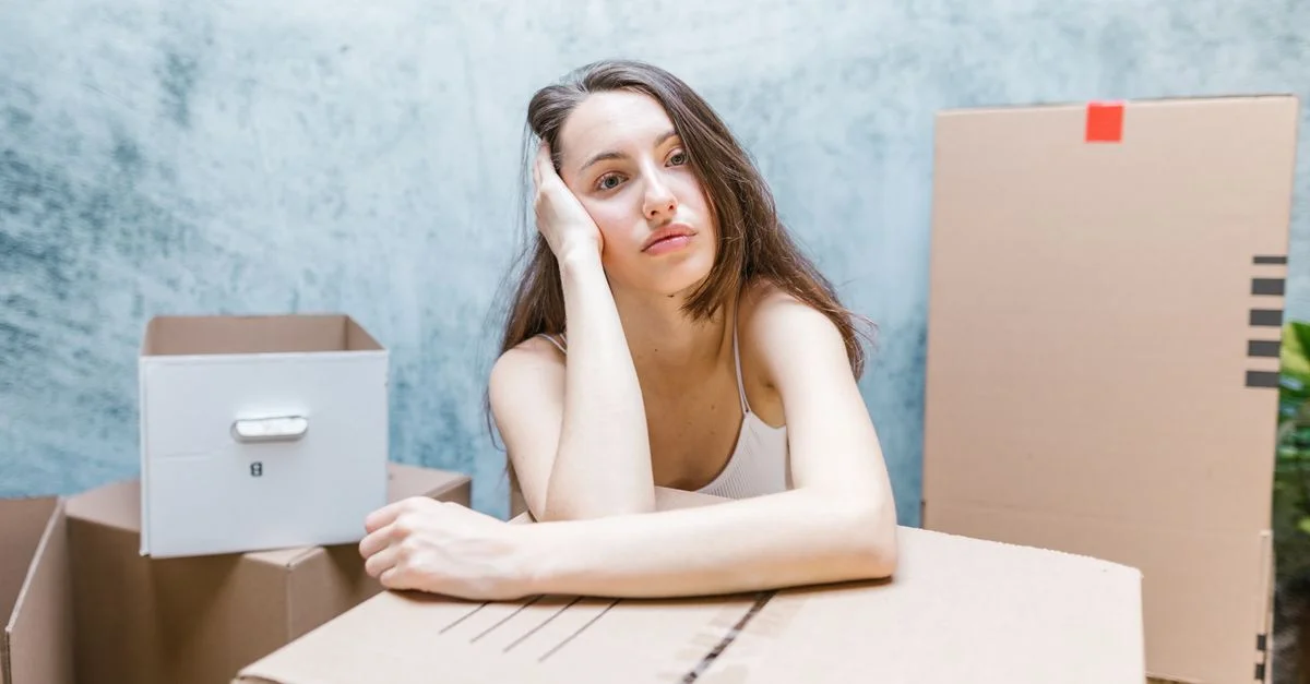 Jeune femme pensive entourée de boîtes de déménagement à l'intérieur.