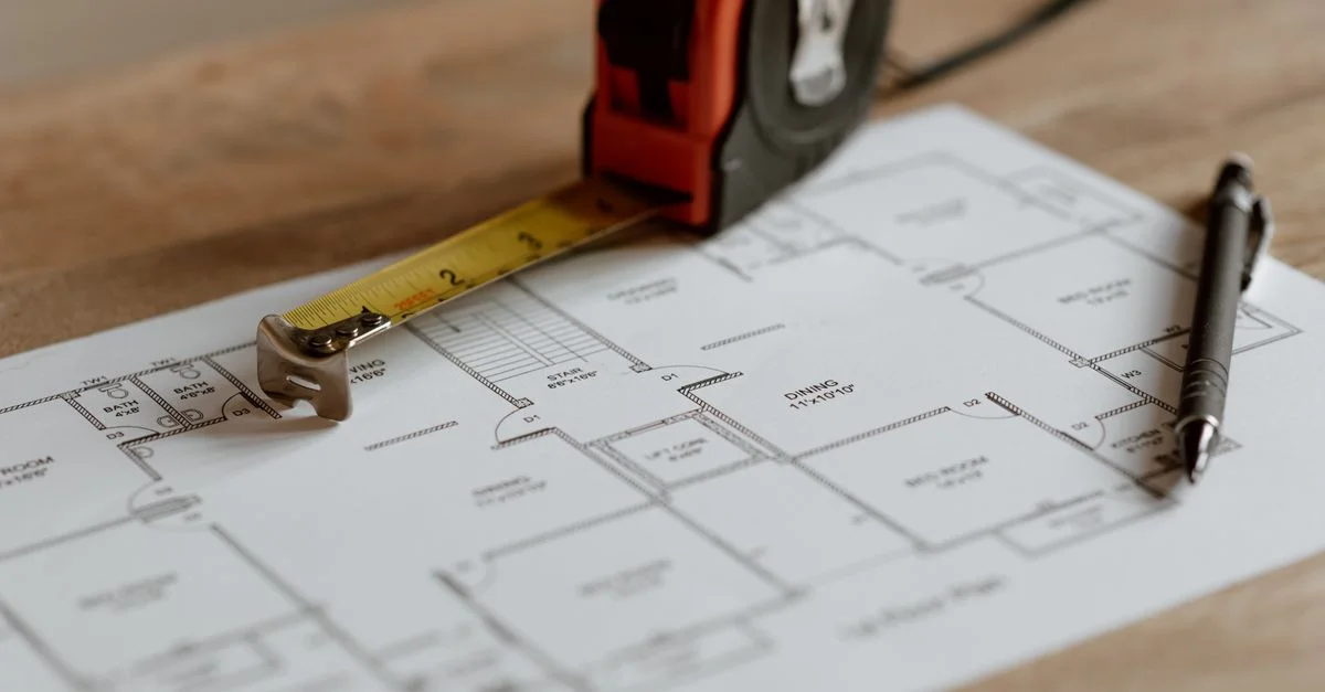 Vue rapprochée de plans architecturaux avec un ruban à mesurer et un stylo sur une table en bois.