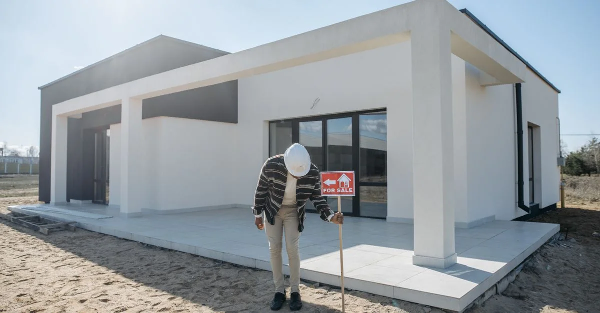 Agent immobilier avec casque debout près d'une maison moderne à vendre.